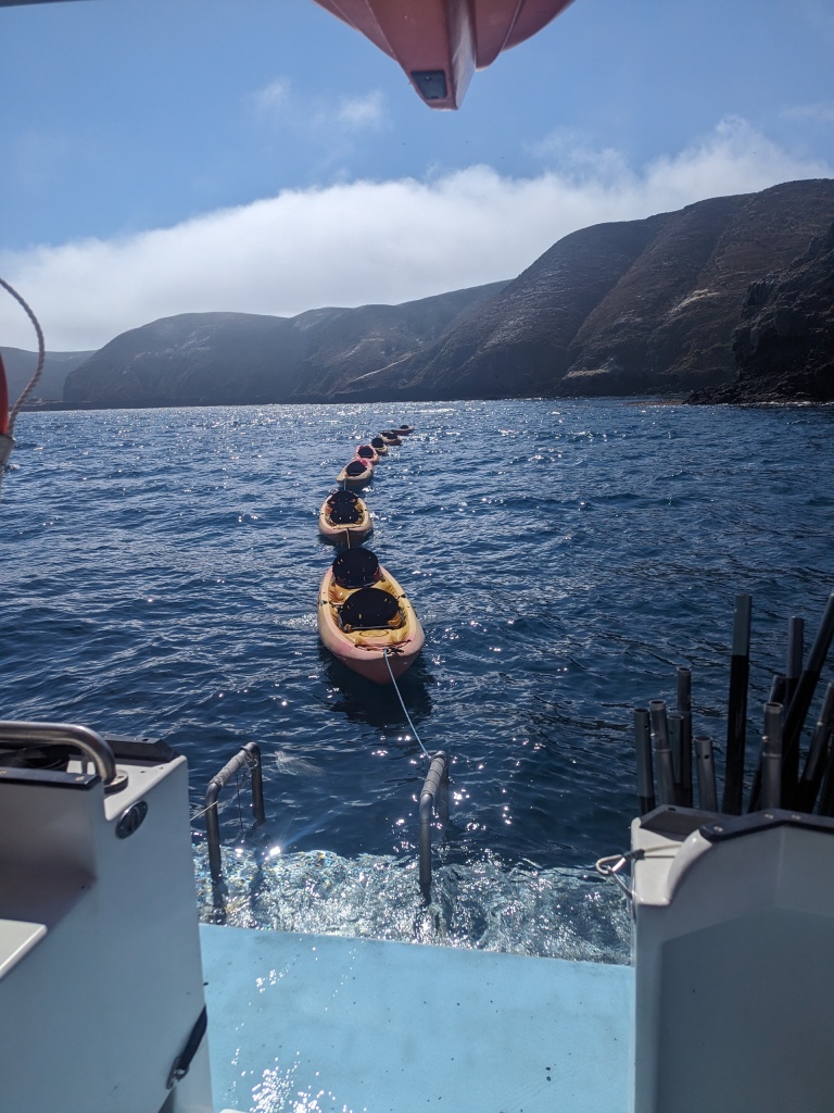 View of open water backing up to Anacapa island with a line of kayaks strung together in the foreground.